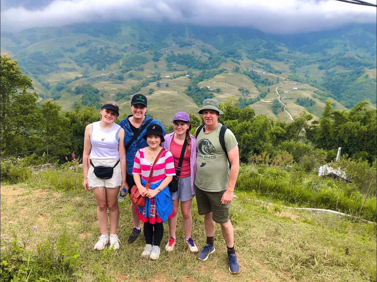 Sapa trekking with a local guide and a group of tourists taking photos in front of terraced rice fields.